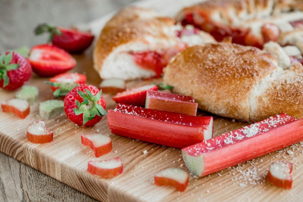 Appetizing homemade sweet pie with strawberries and rhubarb served on wooden cutting board with berries on table in light kitchen