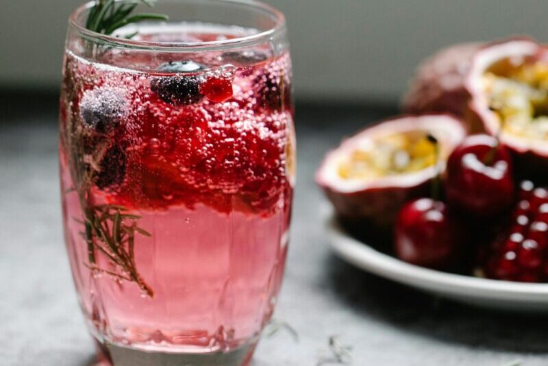 A sparkling pink berry drink garnished with rosemary, perfect for a refreshing treat.