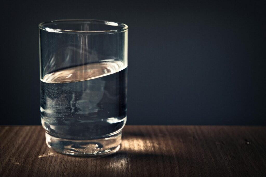 A clear glass of water sitting on a wooden table against a dark background.