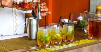 Bartender pouring rum into cocktail glasses at a vibrant bar setting.