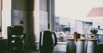 Cozy kitchen scene with coffee maker, kettle, and jars on a sunny counter.