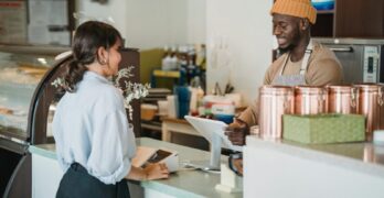 A barista and customer enjoy a friendly interaction at a café counter with a warm ambiance.