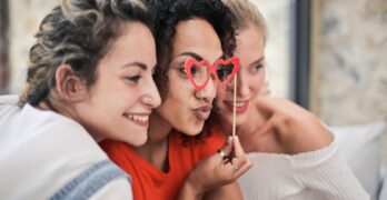 Three women enjoying a playful moment with heart-shaped glasses, symbolizing friendship and fun.