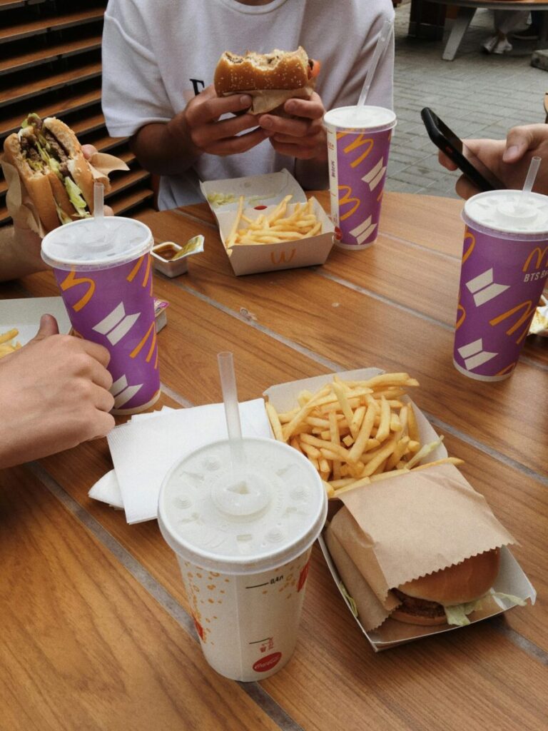 Group of friends enjoying burgers and fries with drinks at an outdoor fast food table.