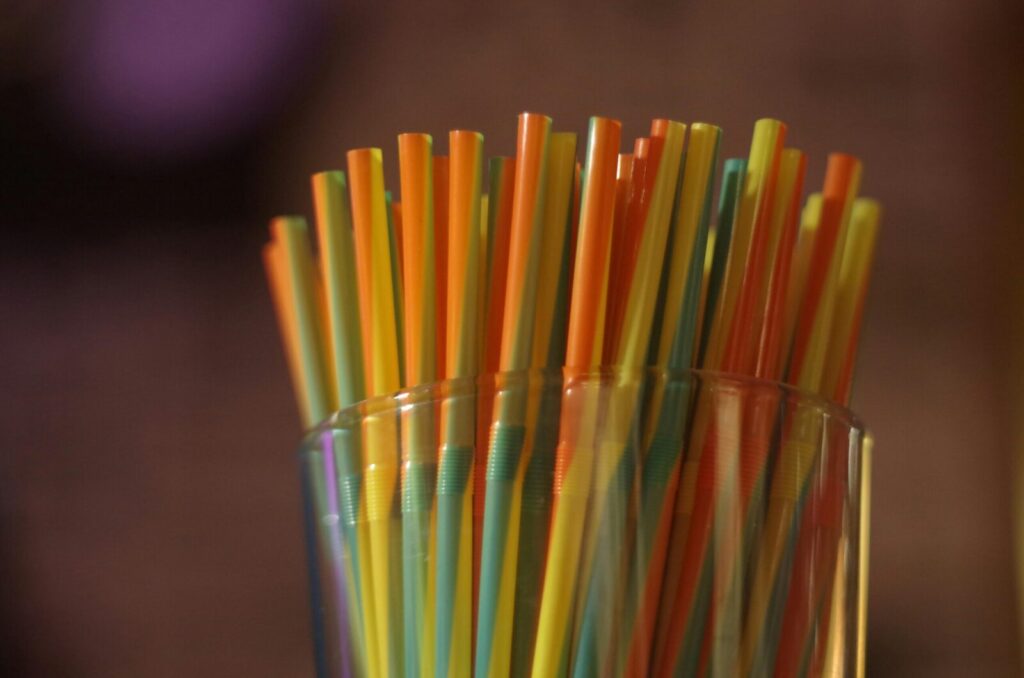 Colorful plastic straws stacked in a glass with a blurred background, highlighting vibrant hues.