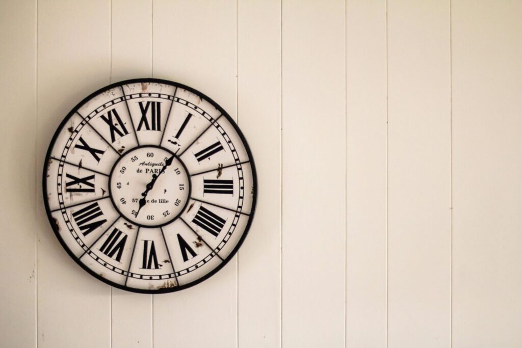 Retro wall clock with Roman numerals on a white wooden background.