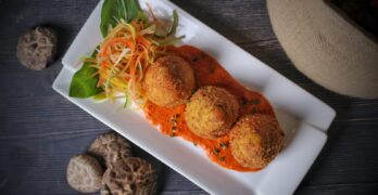 Italian arancini served with tomato sauce and fresh vegetables in a top view presentation.
