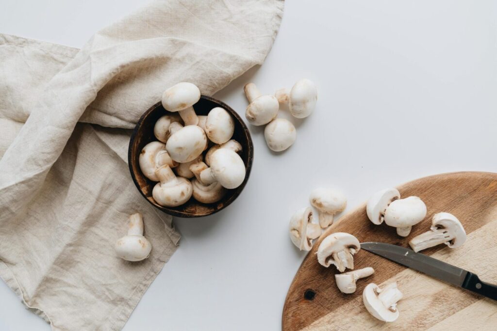 Close-up of fresh white mushrooms on a cutting board with a knife, ready for cooking.