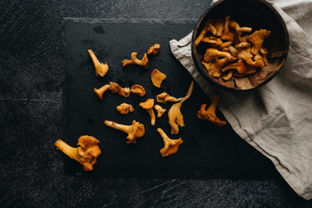 Top view of fresh chanterelle mushrooms on a rustic dark surface with a wooden bowl.