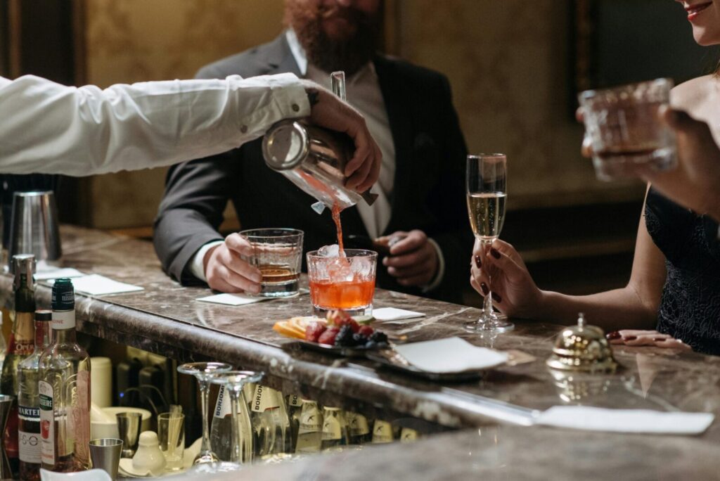 A bartender serves cocktails to well-dressed patrons in an upscale bar setting.