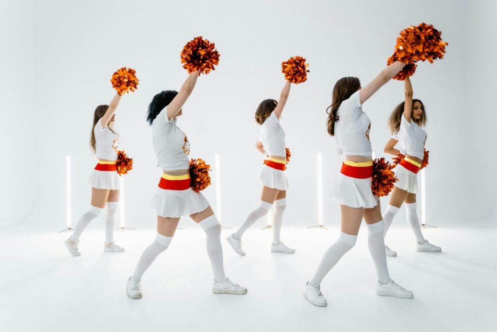 Group of female cheerleaders in matching uniforms performing a routine with pompoms in a bright studio.